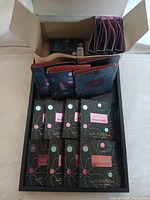 Top view of open box showing multiple sample packs of perfume in black packaging with colorful circles and swirl design, pink Britney Spears label.