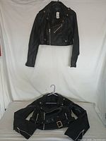 Photo of two black women’s crop jackets hanging and folded, showing overall design and cut