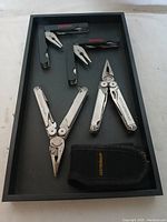 Four Leatherman multi-tools displayed in a black tray including two Wave and two Skeletool models, one with black fabric carrying case.