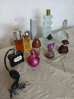 View of all 11 assorted used perfume bottles arranged on white surface showing variety in shapes and colors