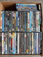 Top view of assortment of DVDs stacked in a box showing titles and overall lot condition.