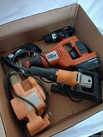 Box with assortment of power tools showing Floor Storm brand cordless drill and several corded tools in orange and black.