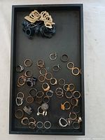 Top-down view of assorted rings laid out in a black tray in multiple metal colors and designs.