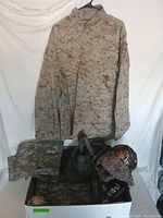 Photo of desert digital camouflage jacket hanging with various other camouflage clothing items and hats arranged below