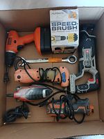 Top-down view of entire lot showing all tools in cardboard box including Black & Decker drill, orange and black corded tools, Speed Brush kit, and ratchet wrench.