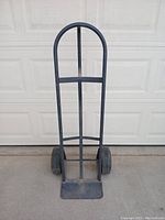 Full front view of the all-metal dolly showing the curved handle, horizontal support bars, flat metal base plate, and pneumatic tires with thick tread.