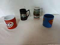 Overview of the four collectible mugs showing Kit Kat, Superman, Budweiser, and a crest design