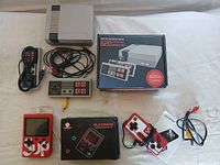 Gaming console, wired controllers, power and AV cables, handheld gaming devices, and original box displayed on white surface