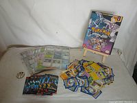 Pokémon trading cards in sleeves, loose cards scattered, and the official scenario guide displayed on an easel.