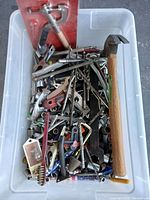Box of assorted small mixed tool bits including various screws, nails, drill bits, and other components with a claw hammer lying on top.