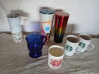 Full lot of Starbucks coffee cups, coffee tumblers and mugs displayed on a table showing all items included in the lot.