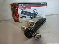 Side perspective showing the hitch with triple trailer balls and original packaging box with branding and specifications.