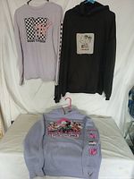 Two sweatshirts hanging on a wall and one sweatshirt laying flat on a table showing designs and colors