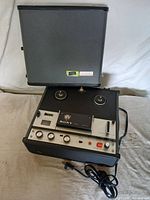 Sony TC-105 open with reels, control panel, power cord visible, and carrying case lid upright behind unit