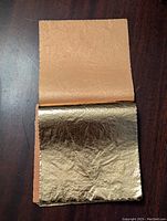Open stack showing a gold leaf sheet on top with its orange backing paper underneath.