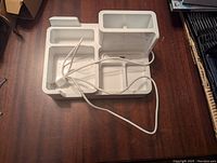 White plastic desk organizer with multiple compartments and an electrical cord placed on a wooden surface, front angle view.