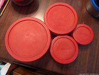 Top view of four red plastic lids of varying sizes stacked on a table, showing the embossed 'Anchor' name on each lid.