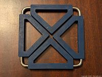 Top view of metal hot plate trivet with rubber padding showing geometric cross design and metal handles.