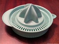 Side-top angled view of the light green plastic manual juicer showing one of the reamers attached and the strainer and container base.
