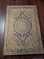 Top view of the large hardcover drawing journal showing the ornate embossed cover design with one metal clasp attached.