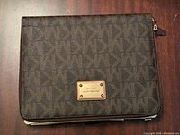 Front view of Michael Kors iPad Air case showing brown signature MK fabric with gold brand plate.