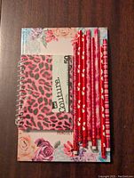 Lot containing a floral gratitude journal, pink leopard print spiral notepad, and ten red Valentine-themed pencils.