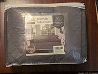 Photo of unopened reversible sofa cover package showing product label and dark gray color side.