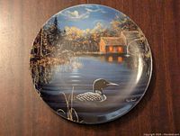Full view of the Serene Sanctuary decorative plate depicting a loon on a lake near a watermill at dusk or dawn with vivid natural scenery.