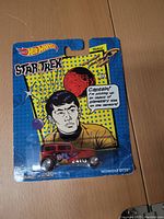 Front view of unopened Hot Wheels Star Trek Sulu Midnight Otto car packaging with comic-style Sulu illustration and blue/yellow background