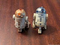 Front angled view of R4-G9 (left) and R2D2 (right) figures on wooden surface showing color and detailed parts.