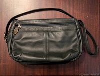 Front view of black leather crossbody purse, showing front zipper compartment and Stoke Mountain charm on zipper pull