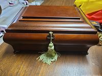 Top angled view of the closed wooden music jewelry box, showing front with key and tassel.