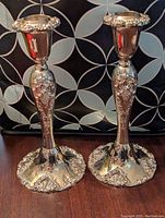 Pair of Godinger silver plated candle holders displayed side by side on a dark wooden surface with a patterned background.