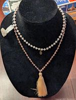 Two long Zacasha beaded necklaces on a black display, one pink with tassel, one black with iridescence