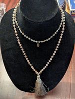 Front view of the necklace with two rows of translucent light beads on display stand, showing the tassel pendant and small charm.