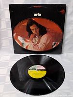 Front view of the vinyl album cover with the record sleeve and vinyl record displayed below it. Shows album artwork with Arlo Guthrie in a pensive pose.