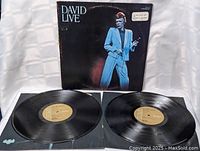 Photo showing the David Bowie Live double album cover and the two vinyl records laid out flat, highlighting the cover image and gold RCA label on vinyl.