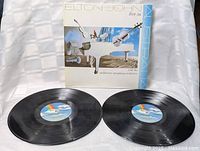 Two black vinyl records laid out flat on a white cloth background.