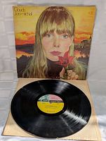 Front cover of the Joni Mitchell Clouds LP record showing artwork with woman holding a red flower and sunset background.