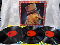 Three black vinyl LP records with red center labels spread out in front of the colorful original album cover featuring Leon Russell.