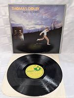Front of record cover with image of man running, vintage audio equipment, and sunset sky background.