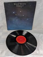 Photo showing vinyl record partially inside album cover with visible night sky star design and vinyl red label.