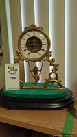 Full front view of clock on green felt base showing cherub pendulum and winding key