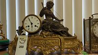 Full frontal view of the antique French mantel clock showing the clock face, figurine of a woman with bow, and the ornate gilt bronze base.
