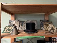 Front view of shelf with beaver top hat in center, multiple worn clock face plates around, brass bell to left, brass snake decor on right.