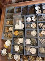 Gray compartment trays with numerous mechanical watch movements and white enamel dials