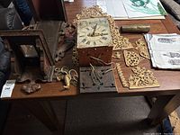 Overall components laid out on table: dial, case parts, carved supports, gilt panels, chains and pendulum weight