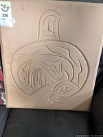 Top view of a carved wooden panel with a killer whale design in traditional Indigenous style.