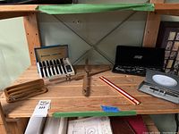 Overview of the lot on a wooden table showing all items: geometry set case, wooden pen set, Staedtler Mars-700 pen set, Parker pen box, wooden protractor and slide ruler.