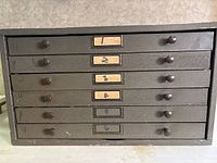 Front view of black metal six-drawer cabinet showing numbered label slots and wooden knobs